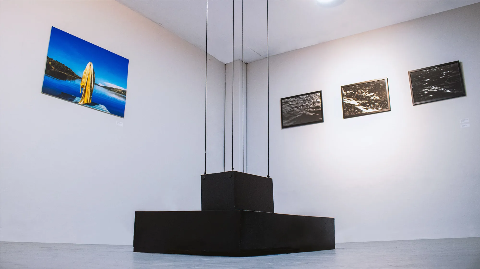 Installation view: photographs on a white gallery wall with a black plinth